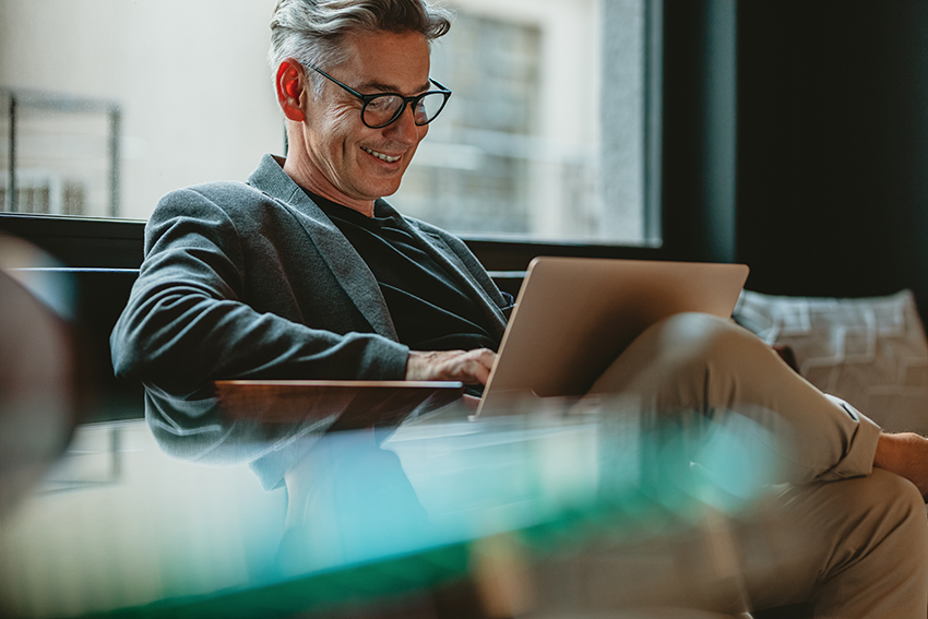 smiling,businessman,sitting,in,office,lobby,working,on,laptop.,male